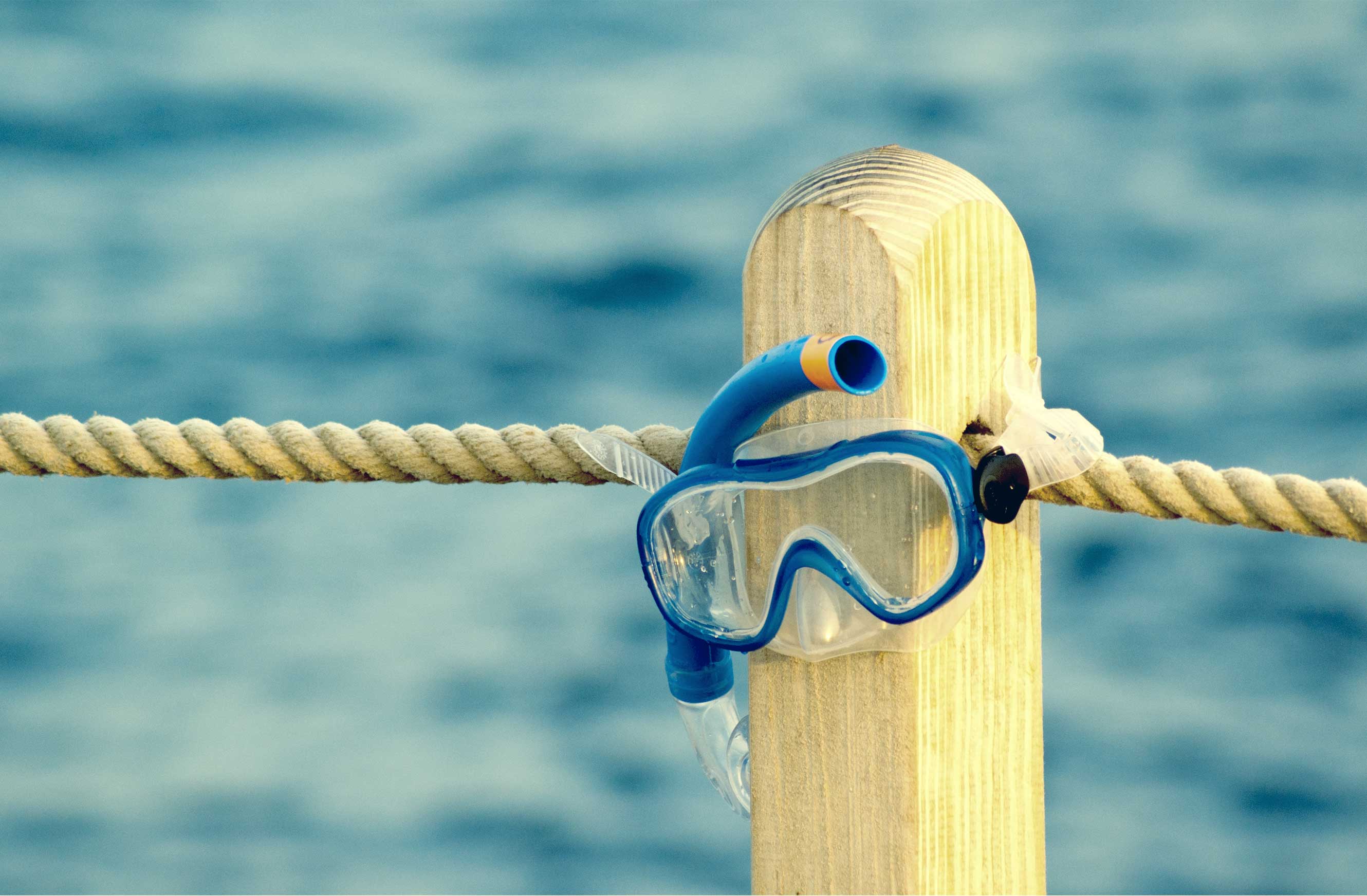 Photo of a mask and snorkel hanging off a wooden post on a pier
