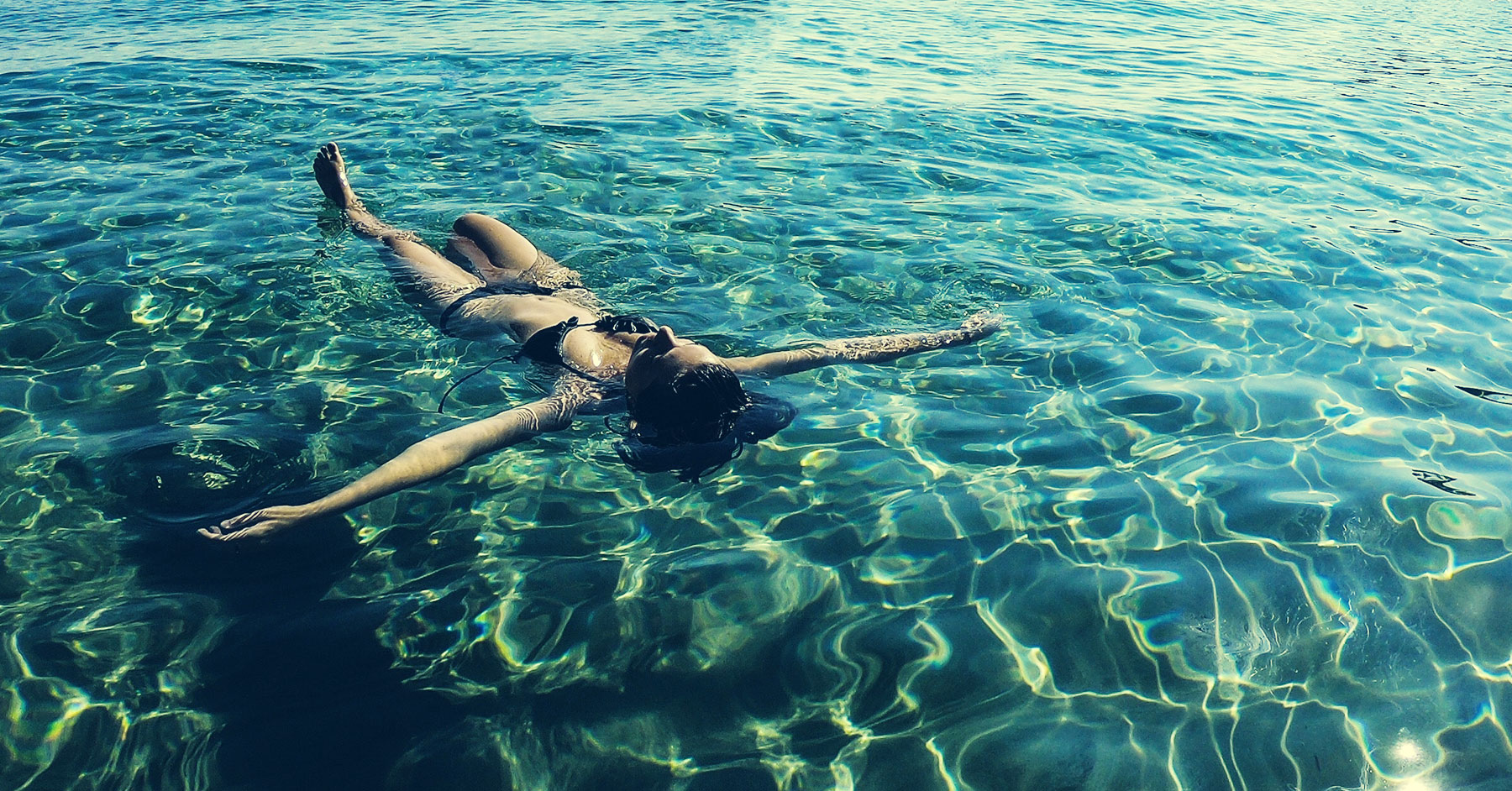 Photo of a woman in a bikini floating on her back in shallow waters