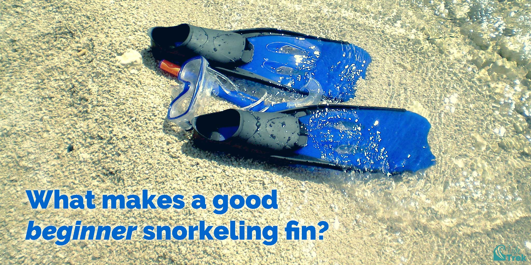 Photo of a pair of snorkeling fins, a mask, and a snorkel in the sand with water washing over them. Text reads, What makes a good beginner snorkeling fin?