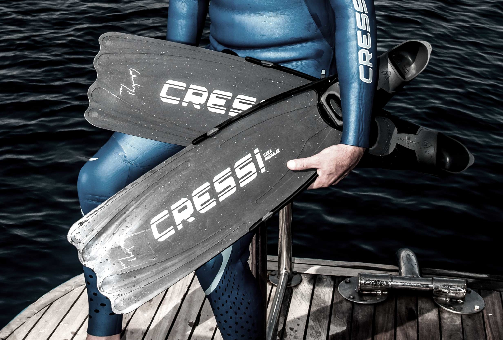Man on a boat deck holding a pair of freediving fins